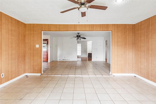 spare room with a ceiling fan, a textured ceiling, wood walls, light tile patterned floors, and ornamental molding