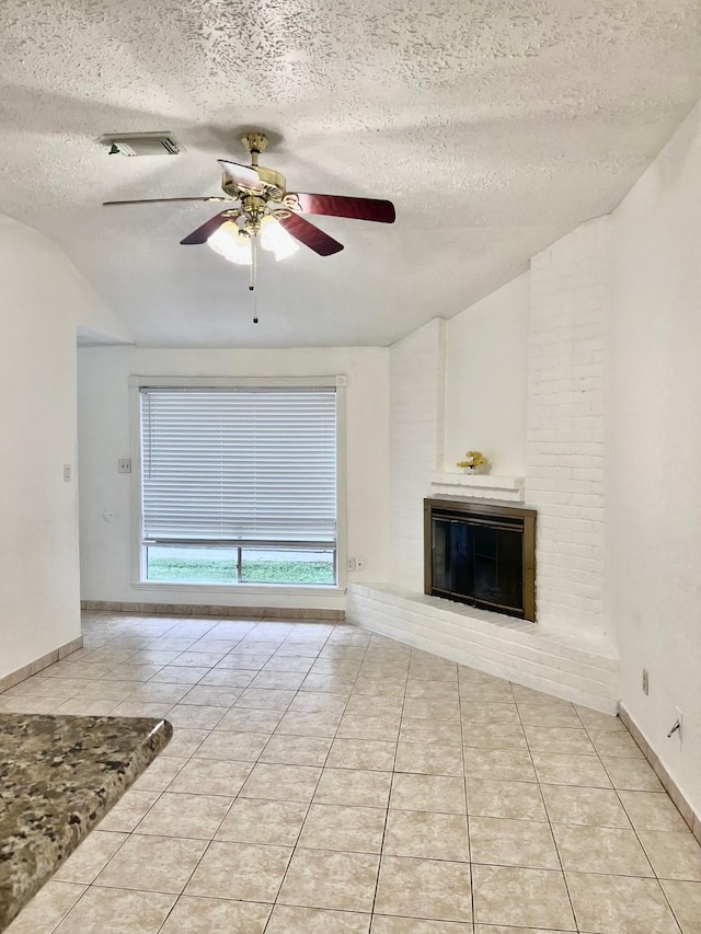 unfurnished living room with a fireplace, a textured ceiling, a ceiling fan, light tile patterned floors, and vaulted ceiling