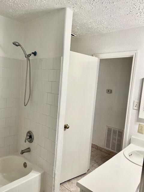 bathroom with shower / bath combination, a textured ceiling, visible vents, tile patterned flooring, and a sink