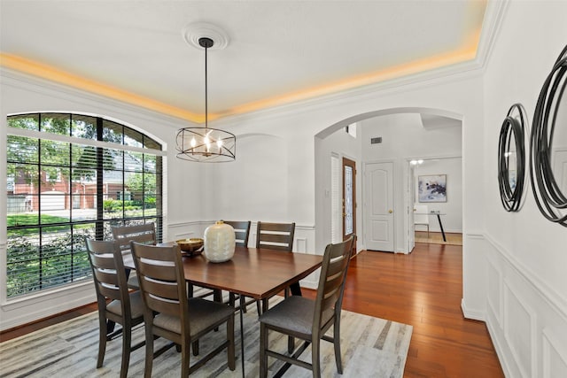 dining room featuring arched walkways, a decorative wall, crown molding, and wood finished floors