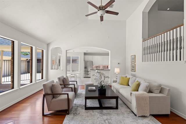 living room with wood finished floors, a ceiling fan, high vaulted ceiling, baseboards, and arched walkways