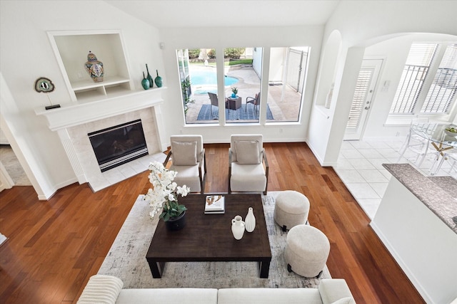 5514 Chase Hbr, Houston, TX 77041 - living room featuring arched walkways, wood finished floors, a tiled fireplace, baseboards, and built in shelves