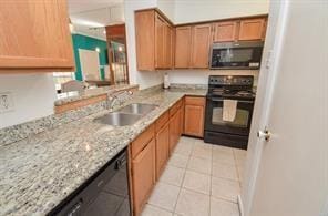 kitchen featuring brown cabinetry, light stone countertops, a sink, light tile patterned floors, and black appliances