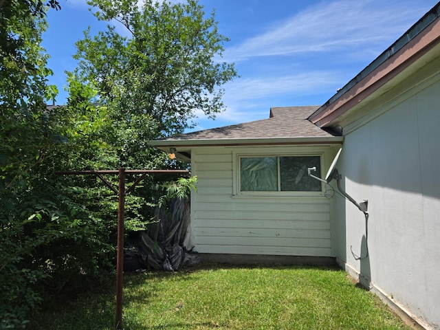 view of side of home featuring a shingled roof and a yard