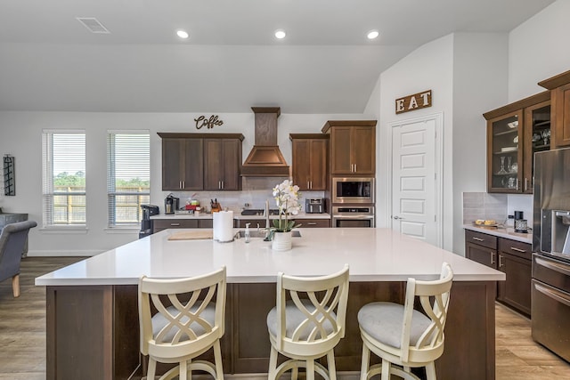 41015 Kimber Ln, Magnolia, TX 77354 - kitchen featuring visible vents, a center island with sink, premium range hood, vaulted ceiling, and stainless steel appliances
