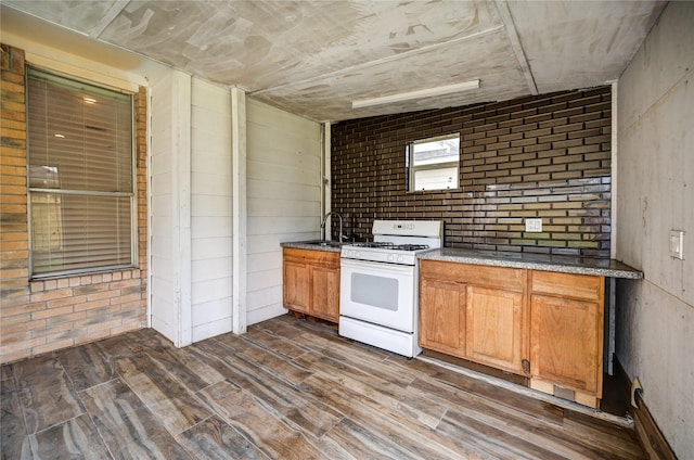 kitchen with dark wood-type flooring, brown cabinets, brick wall, and white gas stove