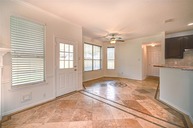 interior space with stone tile floors, a ceiling fan, baseboards, visible vents, and ornamental molding