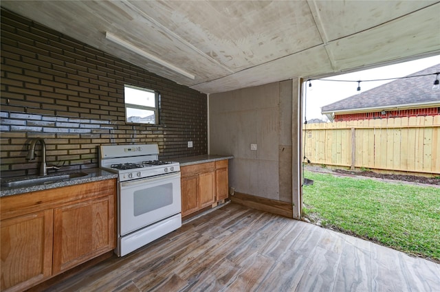 kitchen featuring gas range gas stove, a sink, wood finished floors, and brown cabinets