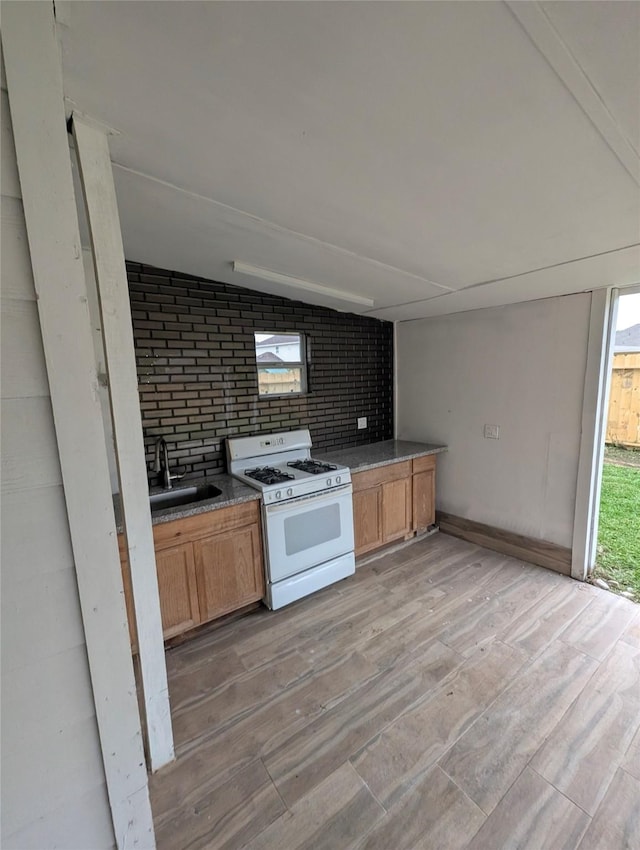 kitchen featuring vaulted ceiling, white range with gas cooktop, a sink, and light wood finished floors