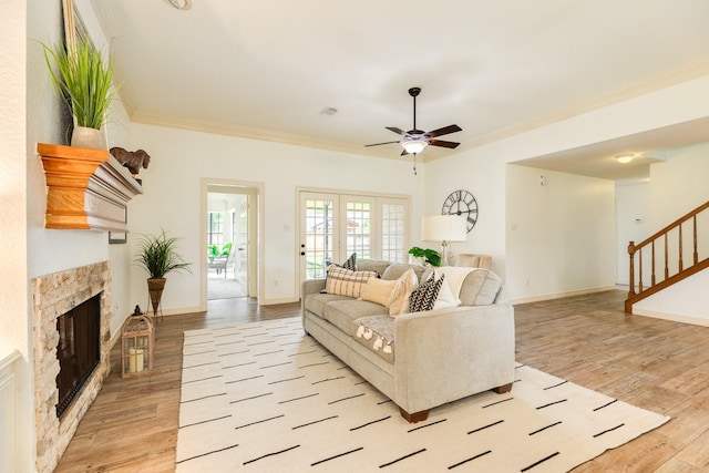 living area with crown molding, ceiling fan, a fireplace, light wood-style flooring, and stairs