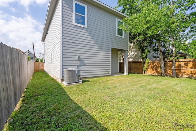 rear view of property featuring a lawn, a fenced backyard, and central AC