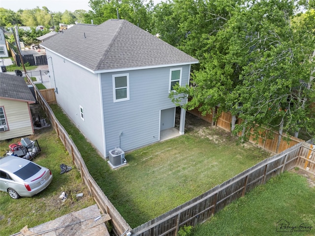 exterior space featuring a fenced backyard, central AC unit, a shingled roof, and a lawn