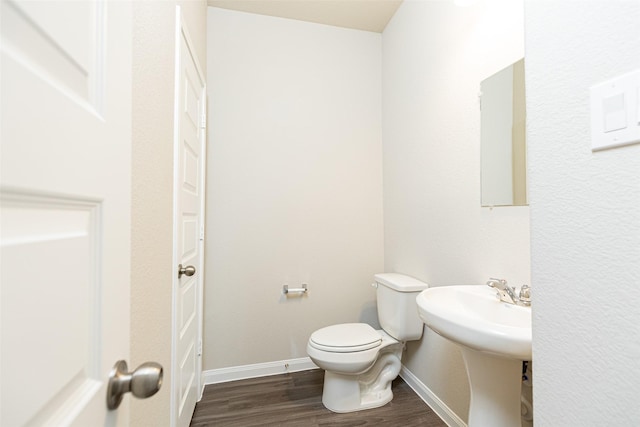 half bathroom with baseboards, wood finished floors, and toilet