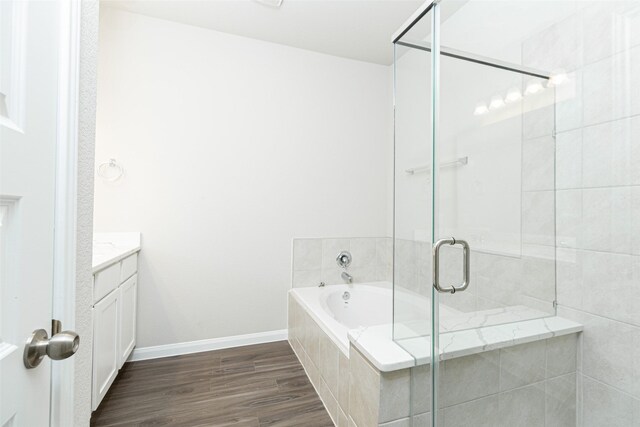 full bath featuring vanity, baseboards, a shower stall, wood finished floors, and a garden tub