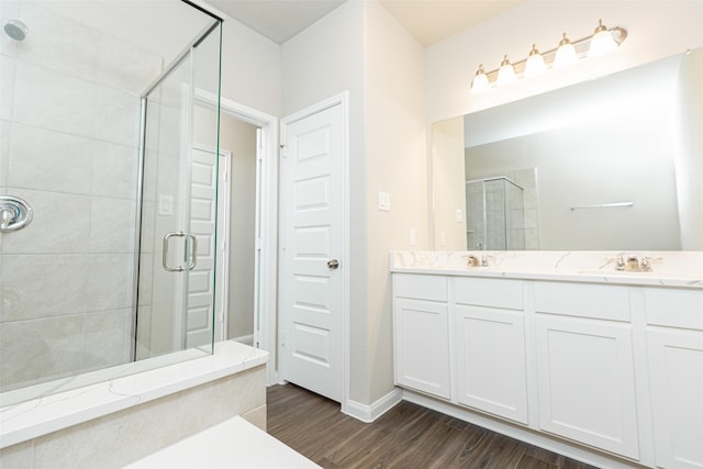 bathroom featuring a sink, double vanity, baseboards, wood finished floors, and a stall shower