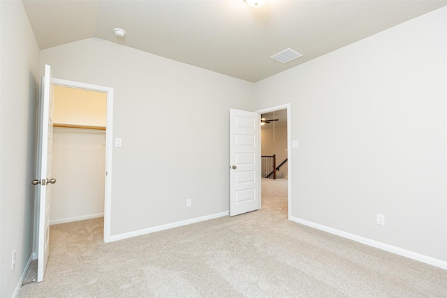 unfurnished bedroom featuring a walk in closet, visible vents, light colored carpet, vaulted ceiling, and baseboards