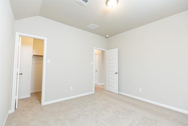 unfurnished bedroom featuring visible vents, vaulted ceiling, baseboards, a spacious closet, and light carpet