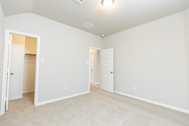unfurnished bedroom with light colored carpet, lofted ceiling, a spacious closet, and visible vents