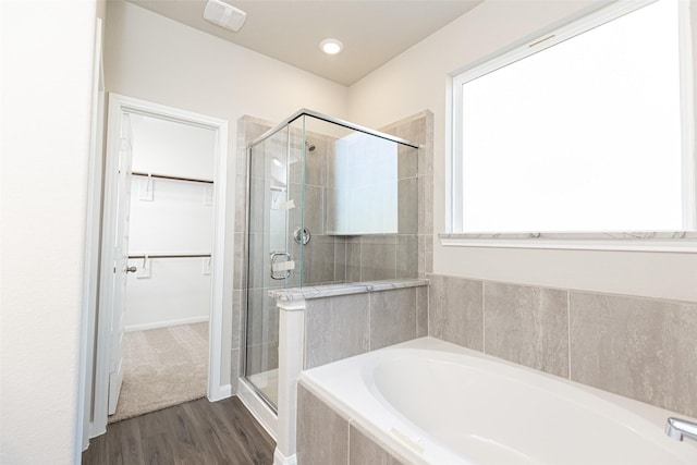 bathroom featuring a walk in closet, a shower stall, wood finished floors, and a garden tub