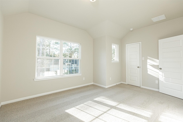 empty room featuring baseboards, vaulted ceiling, and light colored carpet