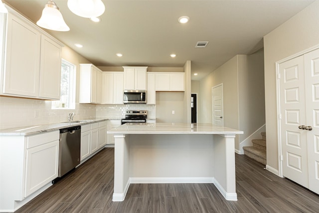 kitchen with dark wood-type flooring, appliances with stainless steel finishes, white cabinets, and tasteful backsplash
