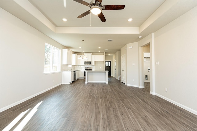 unfurnished living room with baseboards, ceiling fan with notable chandelier, wood finished floors, and a raised ceiling