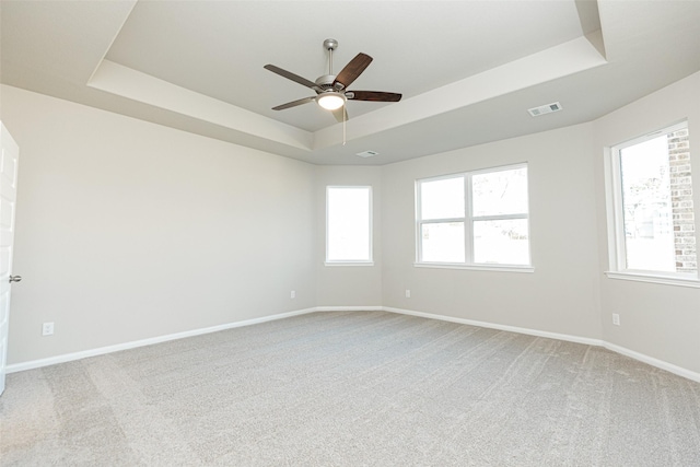 spare room featuring ceiling fan, light colored carpet, a raised ceiling, a healthy amount of sunlight, and visible vents