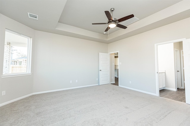 unfurnished bedroom with carpet flooring, a tray ceiling, visible vents, and baseboards
