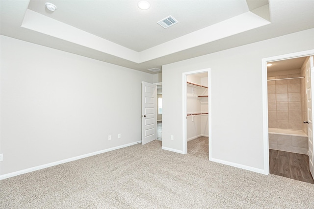 unfurnished bedroom featuring a walk in closet, carpet, a tray ceiling, and visible vents