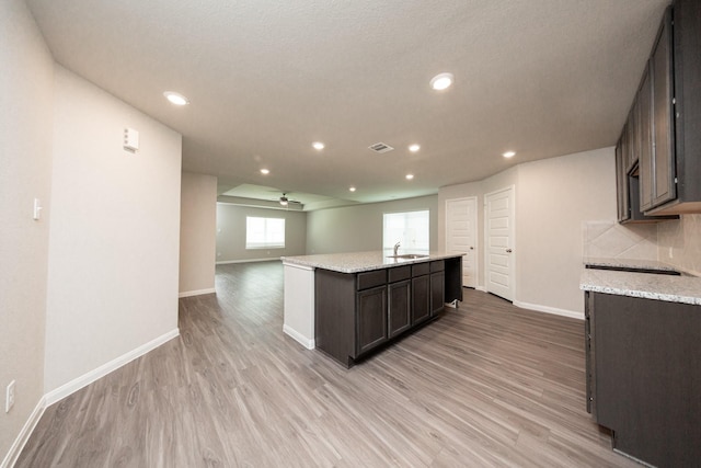 5107 Hector Gustavo Dr, Rosharon, TX 77583 - kitchen with light wood finished floors, an island with sink, dark brown cabinetry, baseboards, and light stone countertops
