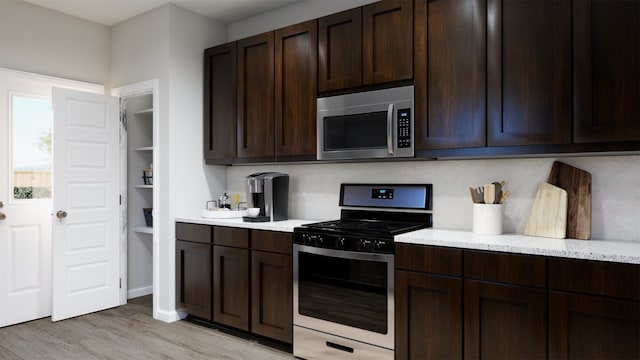kitchen featuring backsplash, appliances with stainless steel finishes, light stone countertops, dark brown cabinets, and light wood-style floors