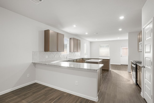 13617 Goldeye Dr, Conroe, TX 77384 - kitchen featuring backsplash, dark wood-style flooring, stainless steel gas stove, baseboards, and a peninsula
