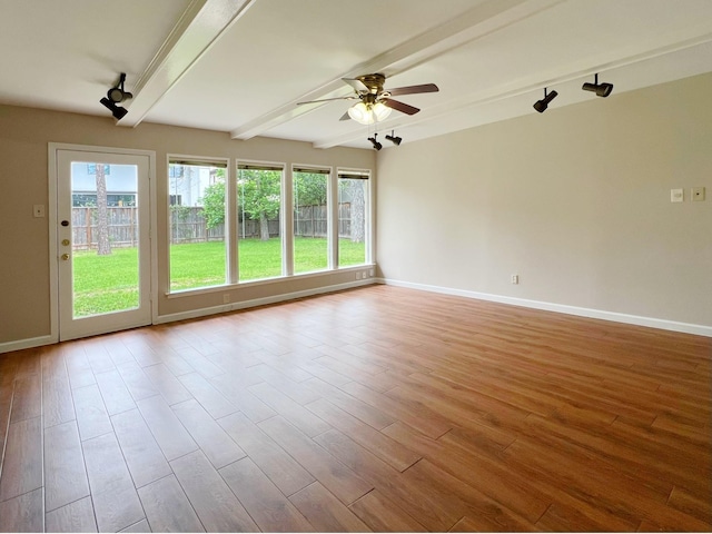 unfurnished room with beamed ceiling, a wealth of natural light, and wood finished floors
