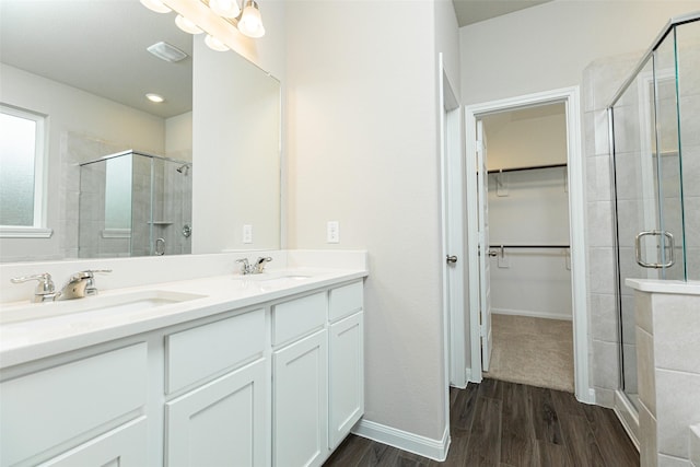bathroom featuring a sink, a walk in closet, wood finished floors, and a shower stall