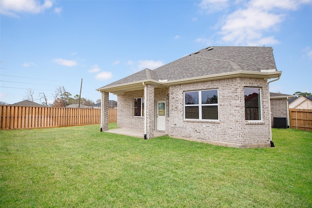 rear view of house with brick siding, a fenced backyard, a yard, and a shingled roof