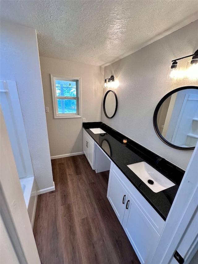full bathroom with double vanity, a bathtub, a textured ceiling, wood finished floors, and a sink