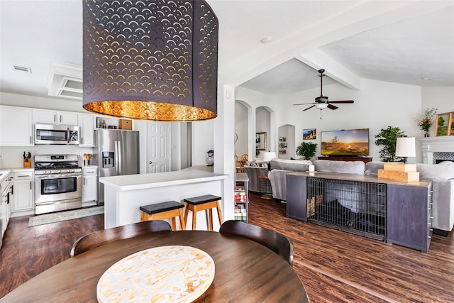 dining room featuring dark wood-type flooring, a ceiling fan, a fireplace, and arched walkways