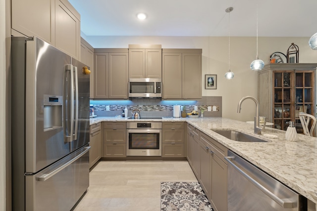 kitchen with pendant lighting, light stone countertops, a sink, backsplash, and stainless steel appliances