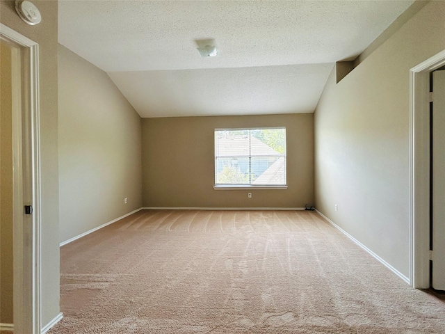 spare room featuring light colored carpet, a textured ceiling, baseboards, and vaulted ceiling
