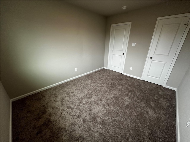 spare room featuring baseboards and dark colored carpet