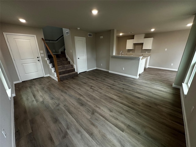 unfurnished living room featuring dark wood-type flooring, recessed lighting, baseboards, and stairway