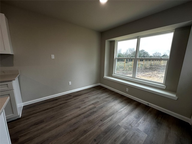 unfurnished dining area with baseboards and dark wood-style floors