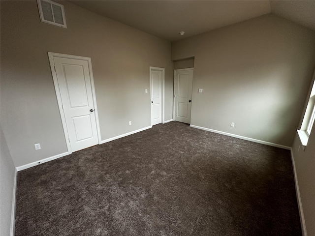unfurnished bedroom featuring baseboards, vaulted ceiling, dark colored carpet, and visible vents
