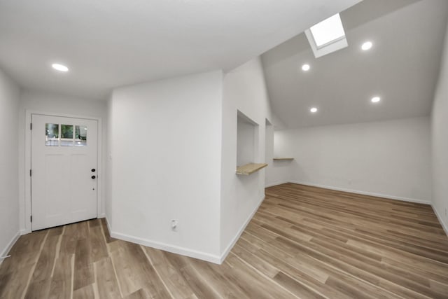 foyer entrance with a skylight, wood finished floors, baseboards, lofted ceiling, and recessed lighting