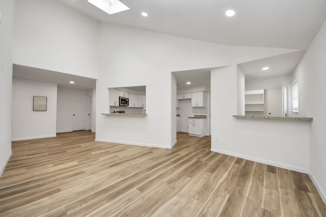 unfurnished living room featuring a skylight, baseboards, light wood finished floors, recessed lighting, and high vaulted ceiling