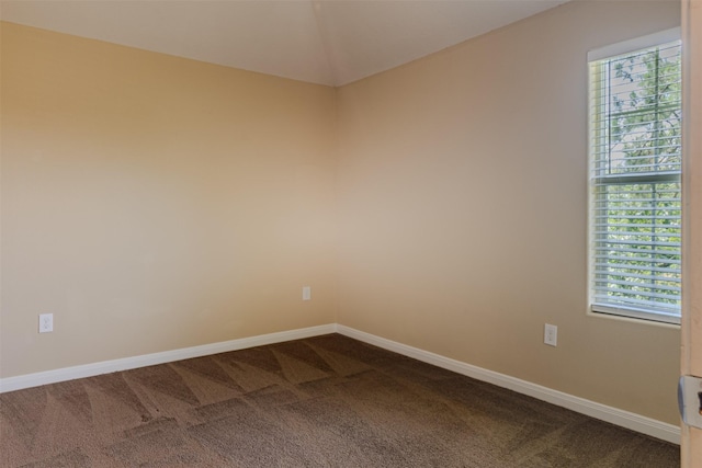 unfurnished room featuring dark carpet, baseboards, and lofted ceiling
