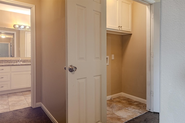 clothes washing area featuring baseboards and a sink