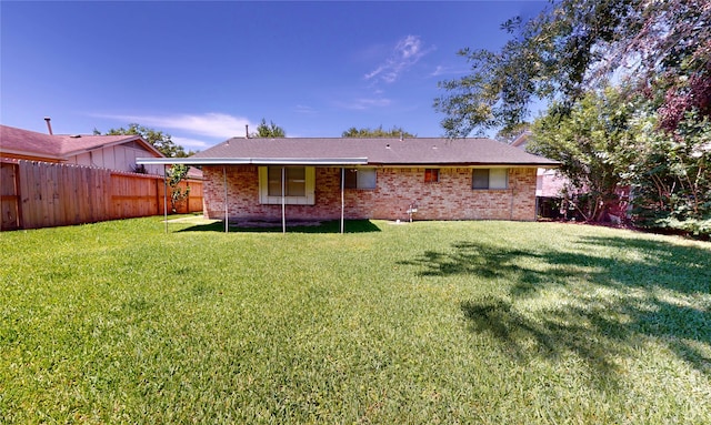 rear view of house featuring a fenced backyard, a shingled roof, a yard, and brick siding