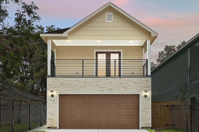 view of front of home with driveway, fence, a balcony, and stone siding