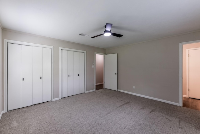 unfurnished bedroom featuring visible vents, carpet, multiple closets, and baseboards